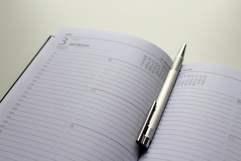 A clinic receptionist looking between a paper day sheet and a shared calendar on screen showing the same time slot